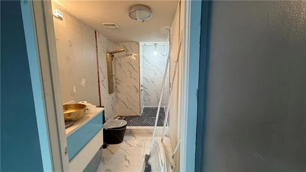 Full bathroom featuring vanity, a marble finish shower, and light marble finish flooring