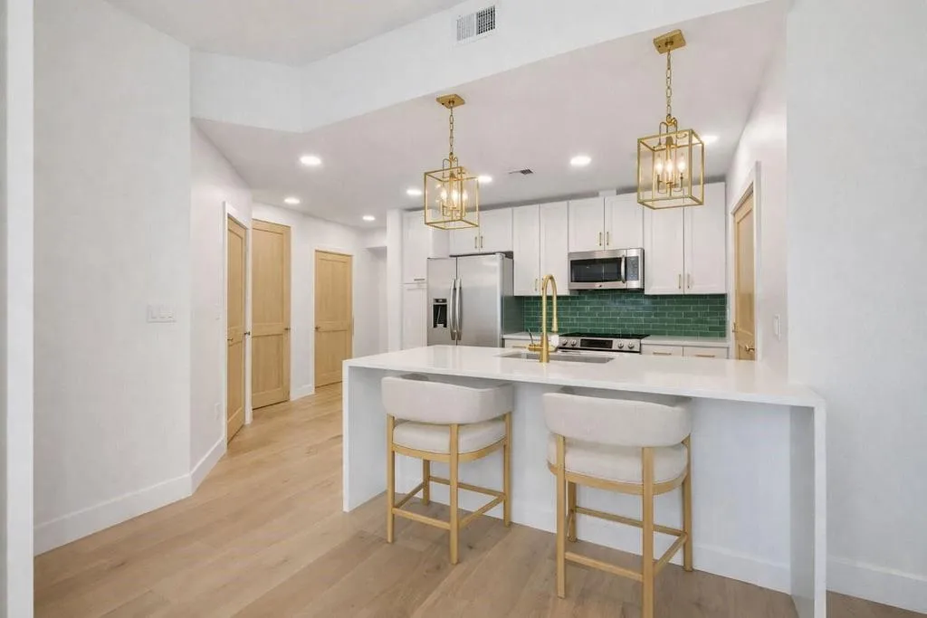 Kitchen with a peninsula, a kitchen bar, light stone countertops, white cabinets, and stainless steel appliances