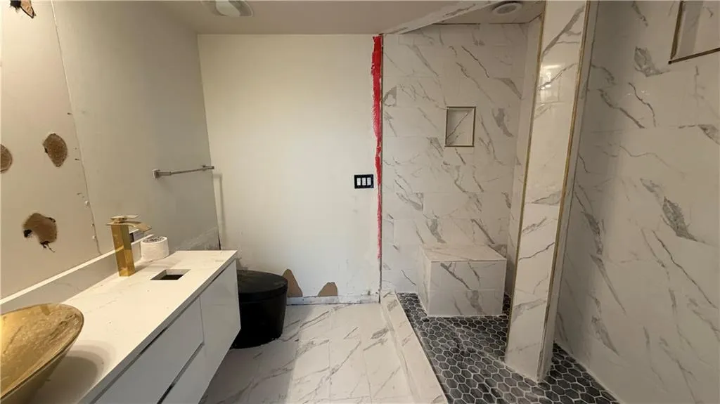 Bathroom featuring light marble finish flooring, vanity, and a marble finish shower