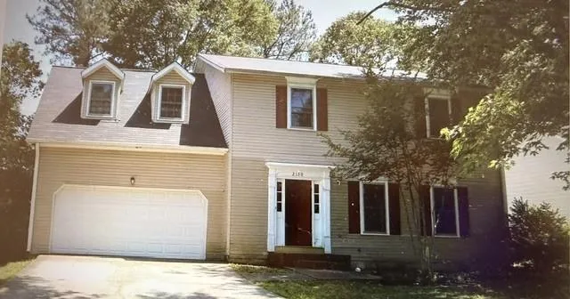 Two-story residence featuring dormer windows, a two-car garage, and red window shutters