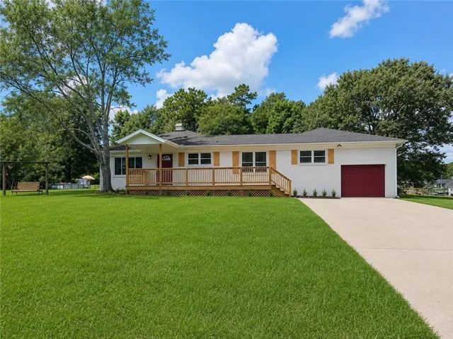 White exterior with a red front door and matching garage door, featuring a spacious wooden deck with railings, and a concrete driveway