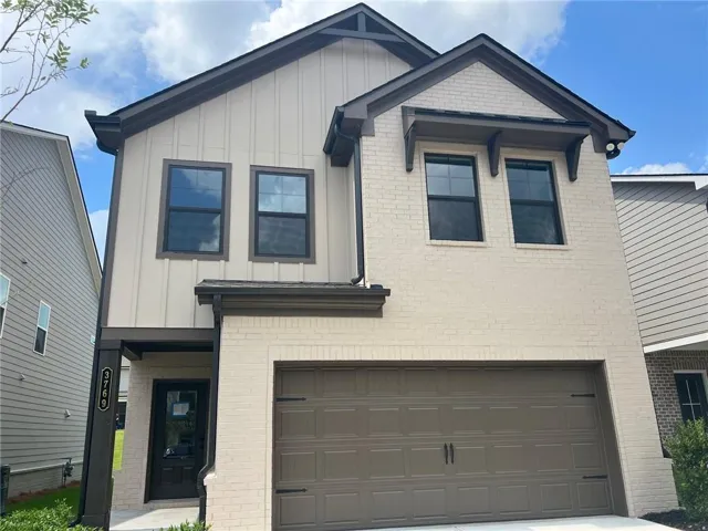 Modern townhome exterior featuring an attached garage, light brick facade, vertical panel siding, dark trim accents, and a covered entry