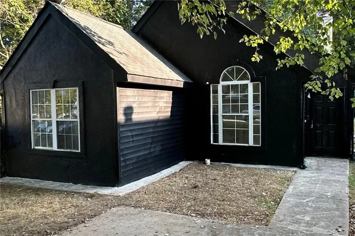 Black exterior finish, arched window with white muntins, white-framed window, dark front door, concrete walkway