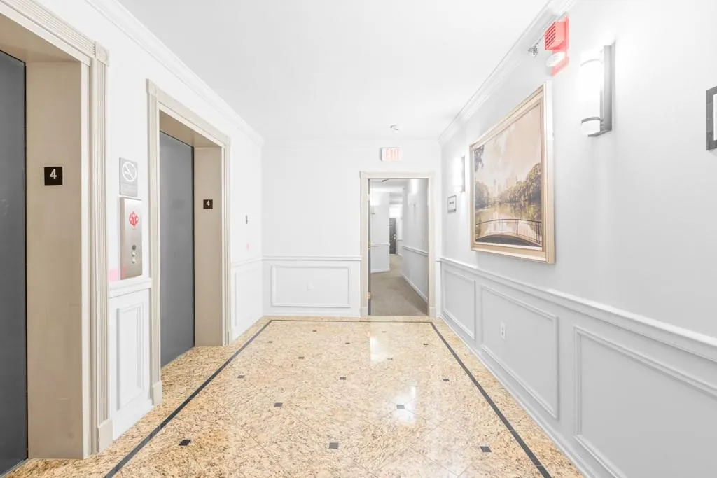 Hallway featuring ornamental molding, a decorative wall, granite finish floor, and a wainscoted wall