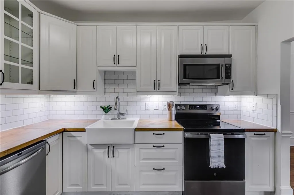 Kitchen with glass insert cabinets, stainless steel appliances, butcher block countertops, white cabinets, and tasteful backsplash
