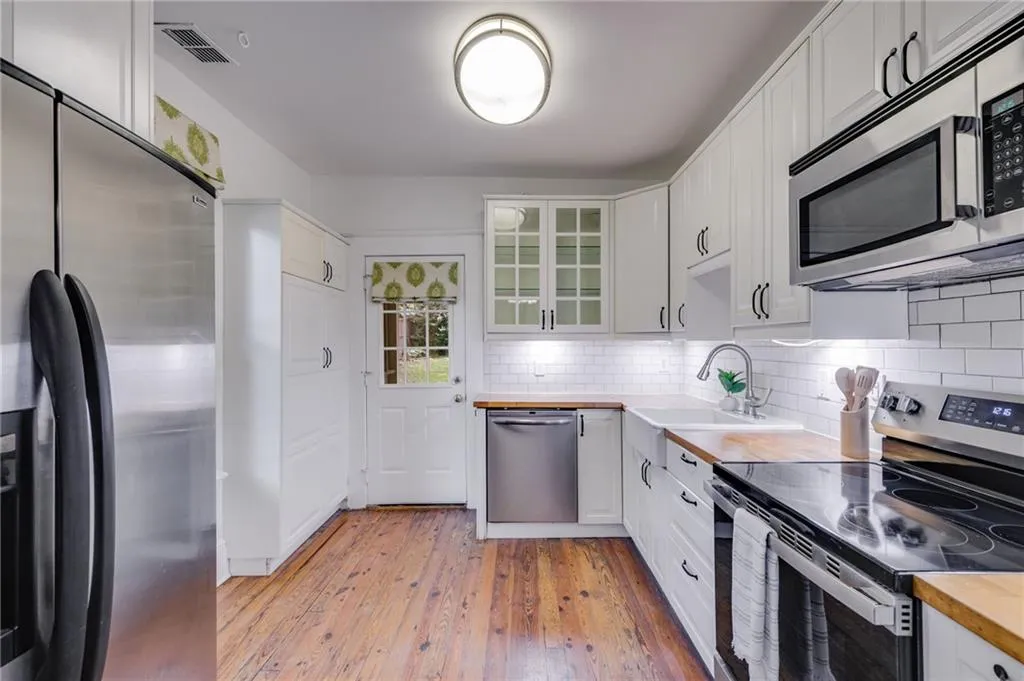 Kitchen with appliances with stainless steel finishes, glass insert cabinets, wooden counters, and white cabinets