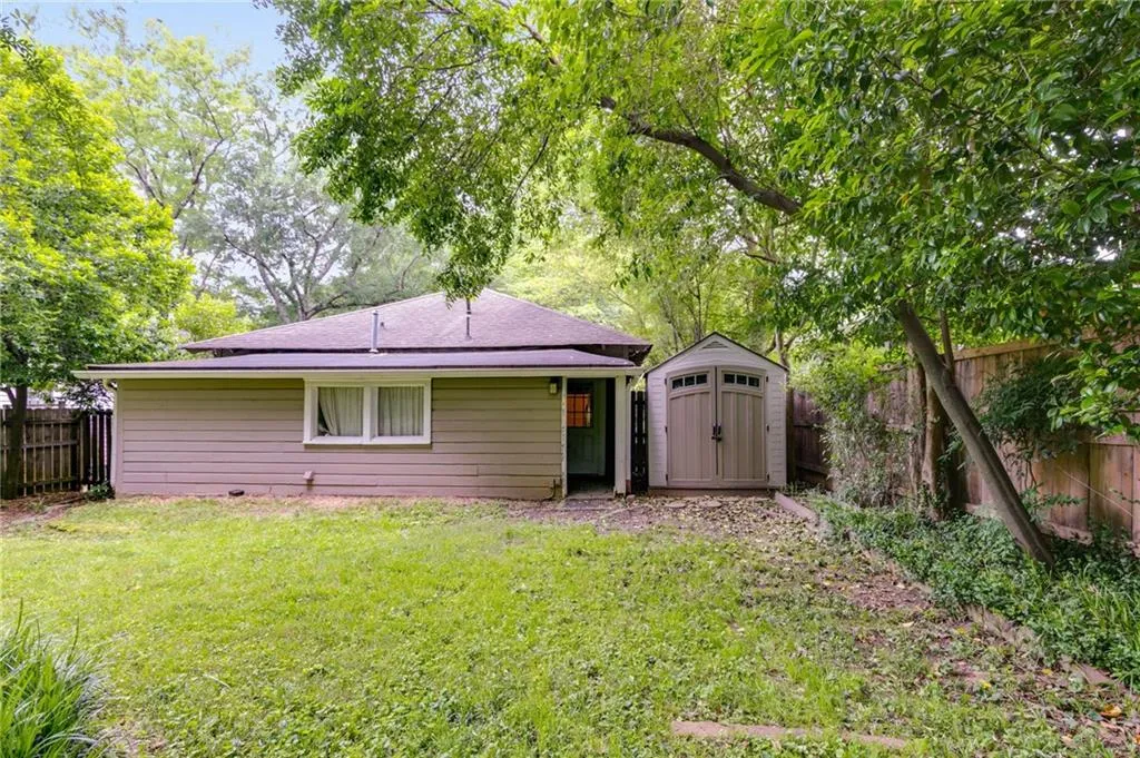 Rear view of house with a fenced backyard, a storage unit, and a shingled roof