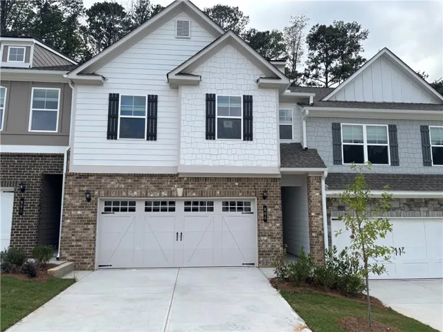 White siding exterior with black shutters, brick accents, two-car garage, and concrete driveway