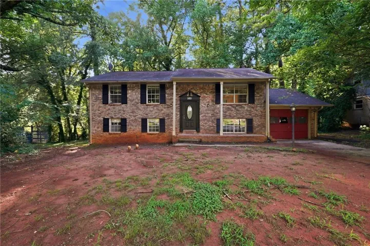 Brick exterior, black shutters, prominent red garage door, asphalt driveway, mature trees