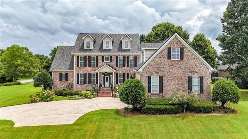 Brick residence featuring a gabled roofline, multiple dormer windows, and black louvered shutters
