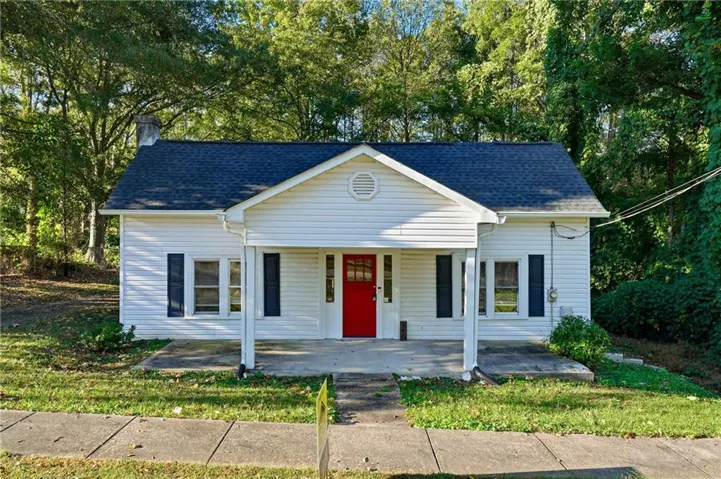 White siding exterior with a prominent red entry door, a covered porch, and dark louvered shutters