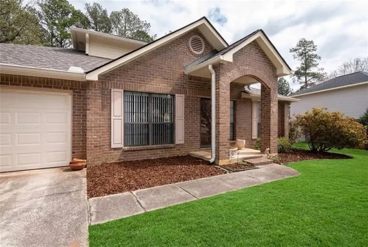 Brick facade with an arched entry porch, a single-car garage, and a manicured lawn