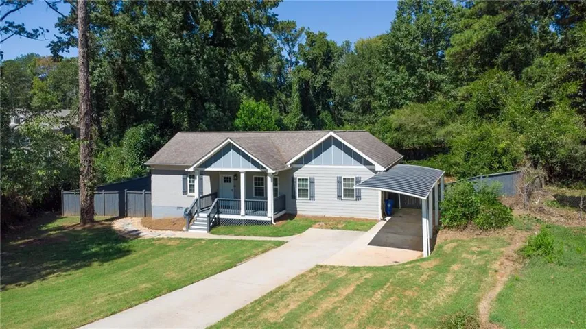 Light gray siding exterior with a covered front porch, a gabled roof, and a paved driveway leading to a carport