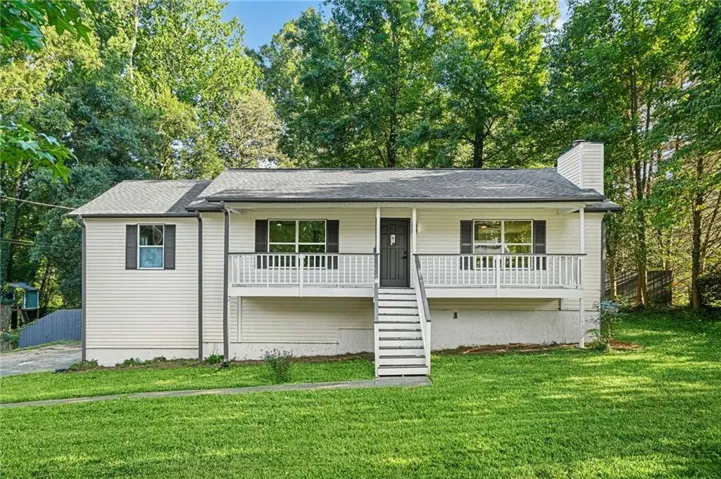 White siding exterior with a dark front door, a front porch with white railing, exterior staircase, and mature trees surrounding the property