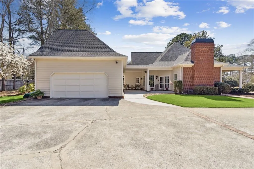 View of side façade featuring the two car garage/carriage house with driveway, roof with shingles, a side lawn, and french doors entry into kitchen area of home.