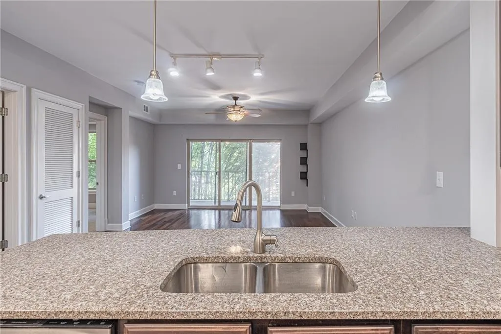 Kitchen with light stone countertops, hanging light fixtures, sink, dishwashing machine, and ceiling fan