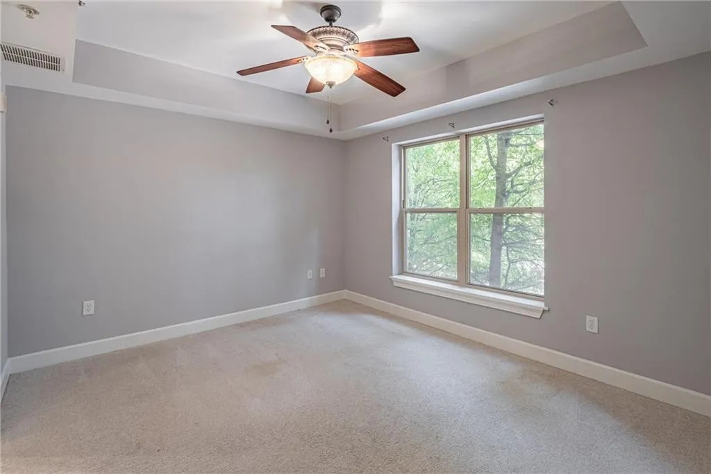 Carpeted empty room featuring ceiling fan and a raised ceiling