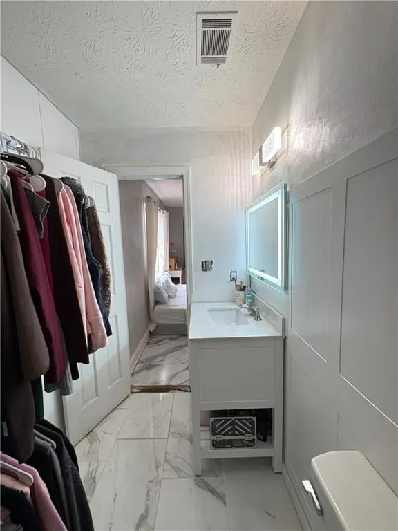 Ensuite bathroom with vanity, light marble finish flooring, and a textured ceiling
