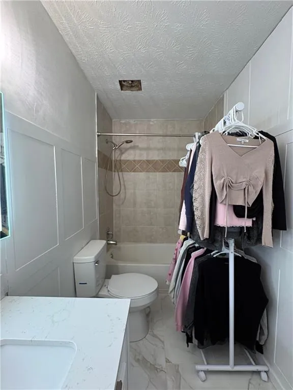Bathroom with a decorative wall, shower / bath combination with curtain, vanity, light marble finish floors, and wainscoting