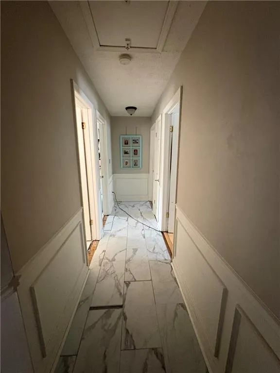 Hallway with a decorative wall, a wainscoted wall, and light marble finish flooring