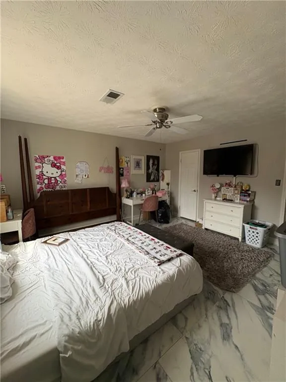 Bedroom with a ceiling fan, marble look tile flooring, and a textured ceiling