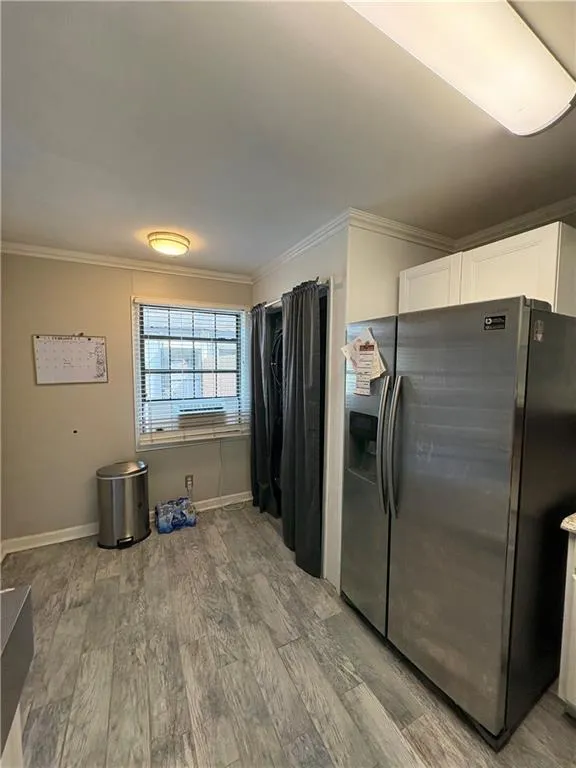 Kitchen with stainless steel fridge, light wood-type flooring, ornamental molding, and white cabinets