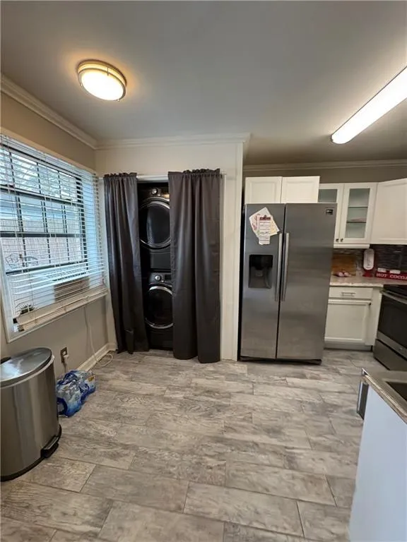 Kitchen with glass insert cabinets, stainless steel appliances, ornamental molding, white cabinets, and stacked washer / dryer