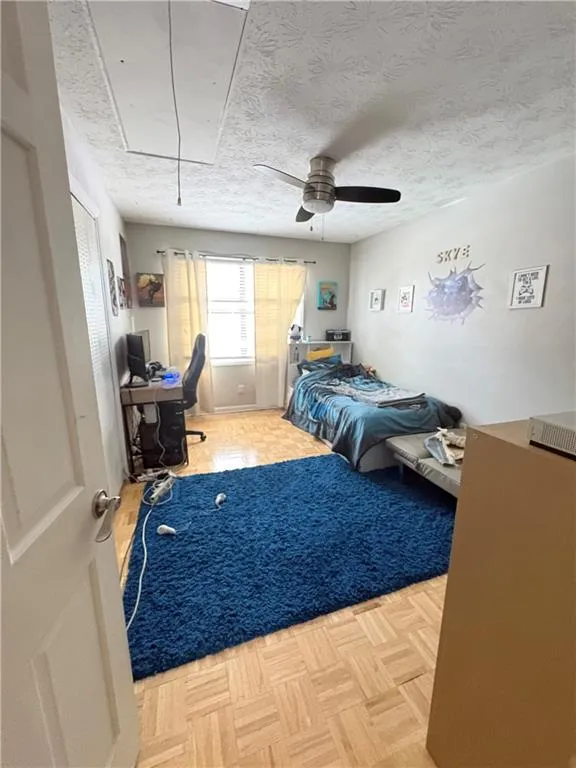 Bedroom featuring a desk, parquet flooring, a ceiling fan, and a textured ceiling