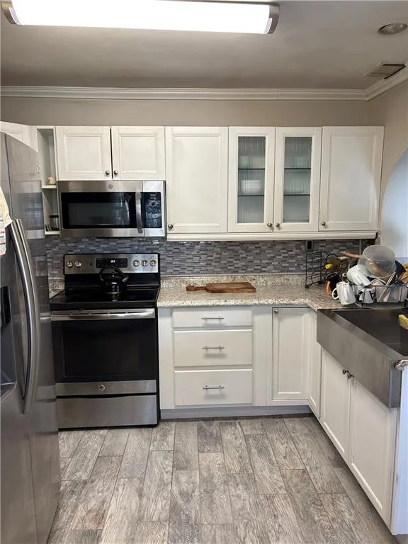 Kitchen with stainless steel appliances, glass fronted cabinets, backsplash, ornamental molding, and light wood-style floors