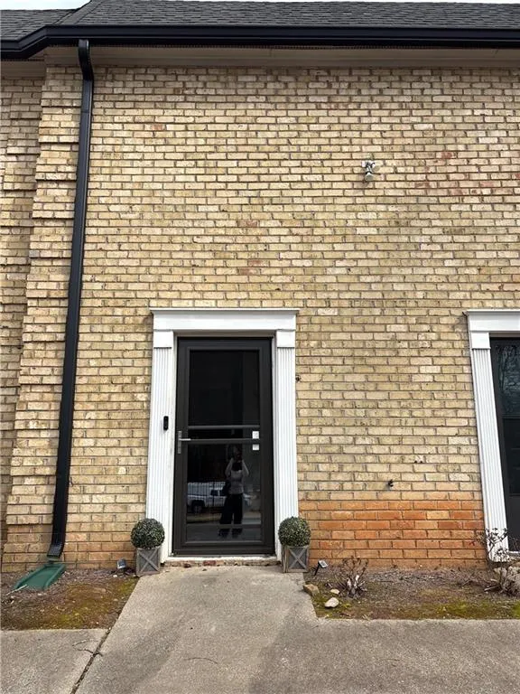 Doorway to property with brick siding and roof with shingles