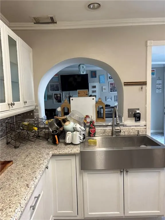 Kitchen featuring white cabinets, glass fronted cabinets, crown molding, light stone counters, and arched walkways