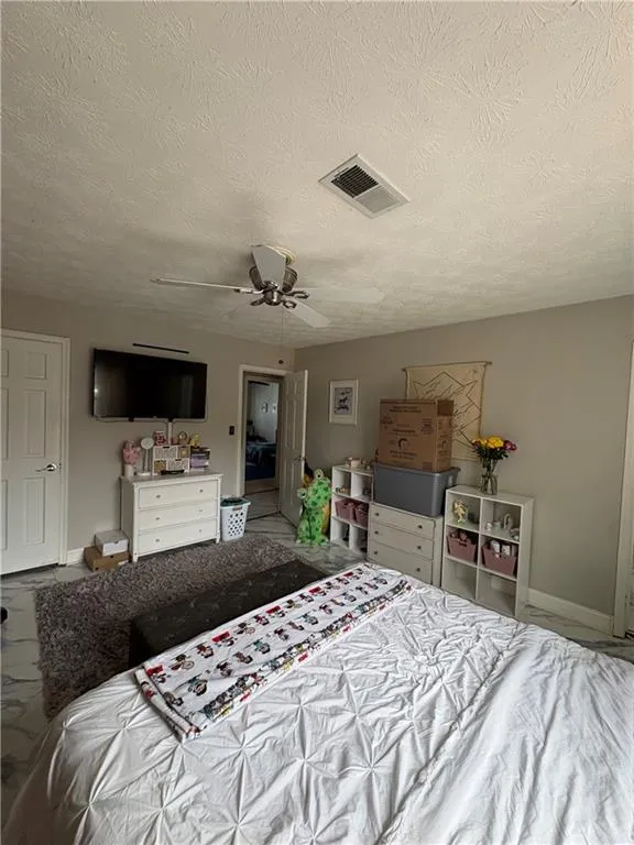 Bedroom featuring a ceiling fan, marble look tiles, and a textured ceiling