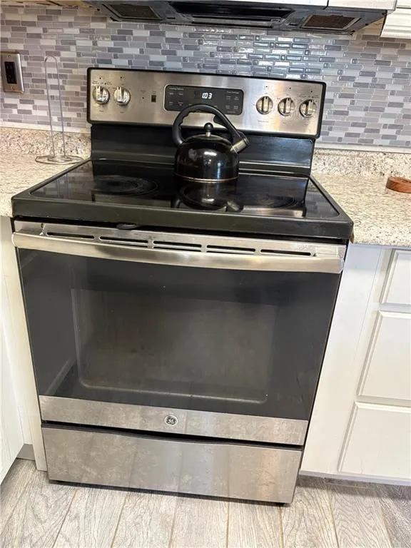 Kitchen view of stainless steel electric range, backsplash, and light stone counters