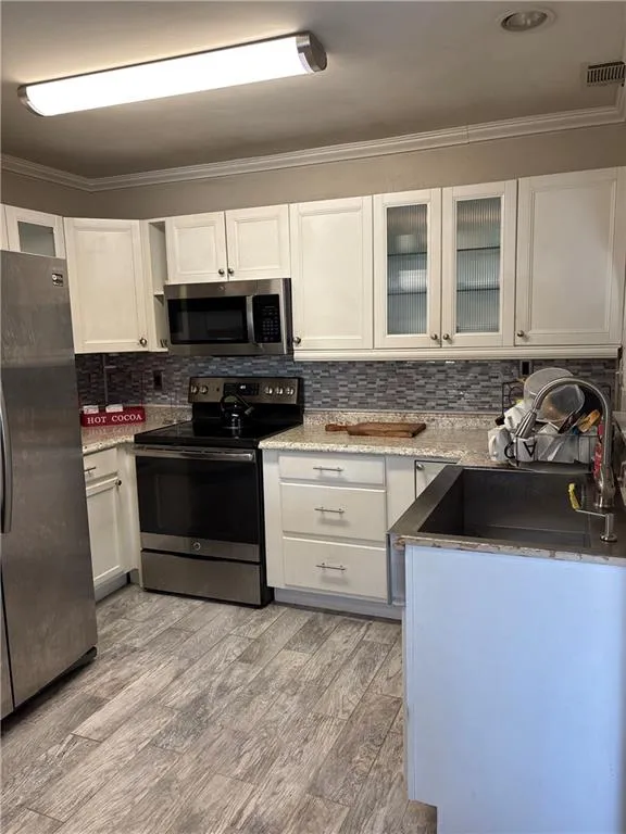 Kitchen featuring glass insert cabinets, stainless steel appliances, decorative backsplash, crown molding, and white cabinets