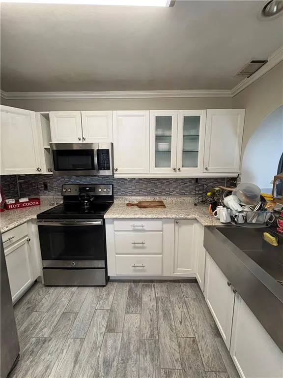 Kitchen featuring stainless steel appliances, white cabinetry, backsplash, crown molding, and light stone counters