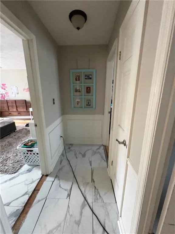 Hallway with light marble finish flooring, a wainscoted wall, and a decorative wall