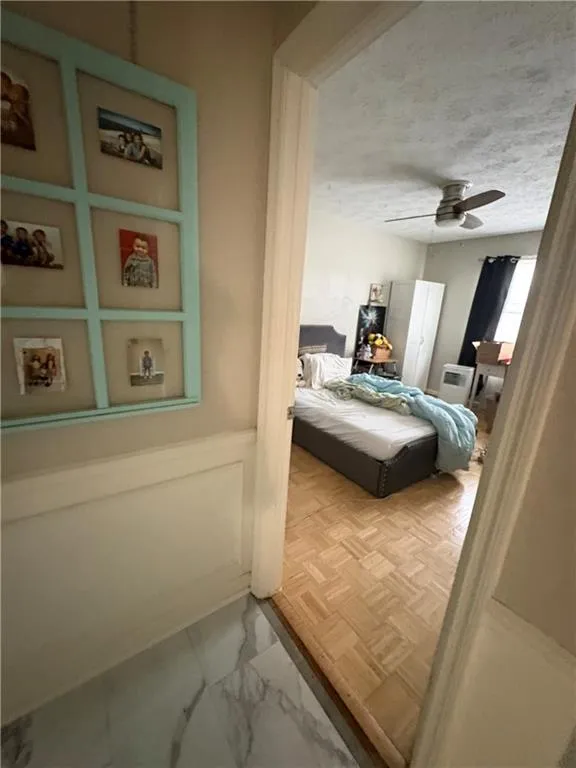 Bedroom with light marble finish flooring, a decorative wall, ceiling fan, wainscoting, and a textured ceiling