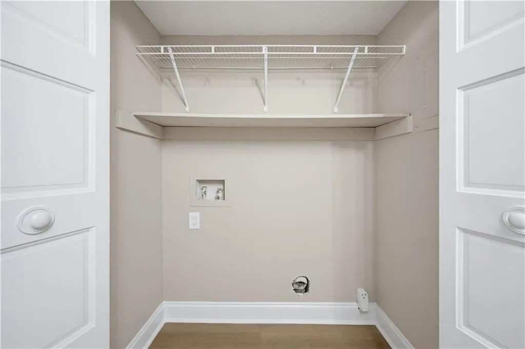 Utility alcove featuring upper shelving, wood-finish flooring, and a laundry hookup