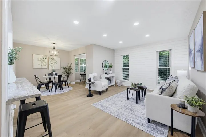 Recessed lighting throughout, wood-finish flooring, dining area with a chandelier, breakfast bar with a stone-finish countertop, and shiplap accent wall