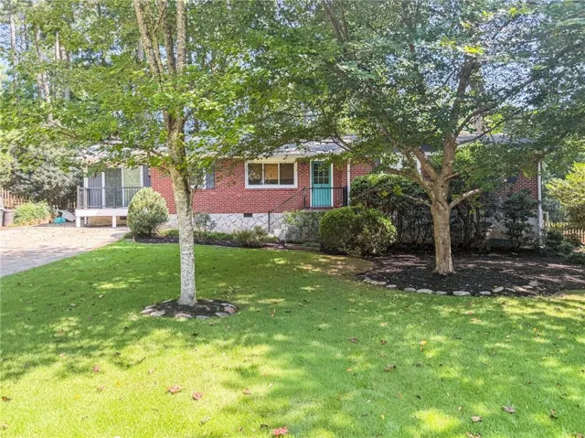 Brick exterior with an accent teal front door, featuring a landscaped front yard with mature trees