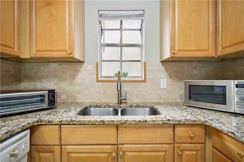 Kitchen with light stone counters, sink, tasteful backsplash, and white dishwasher