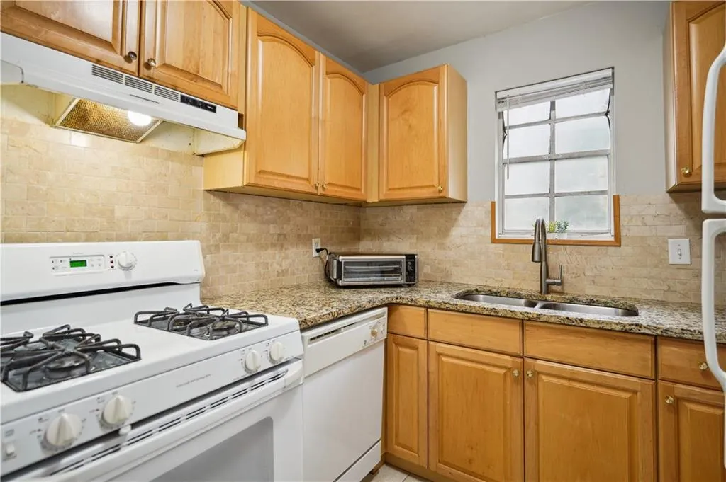Kitchen featuring sink, tasteful backsplash, light stone counters, and white appliances