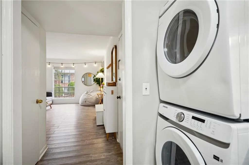Clothes washing area with track lighting, wood-type flooring, and stacked washer / drying machine