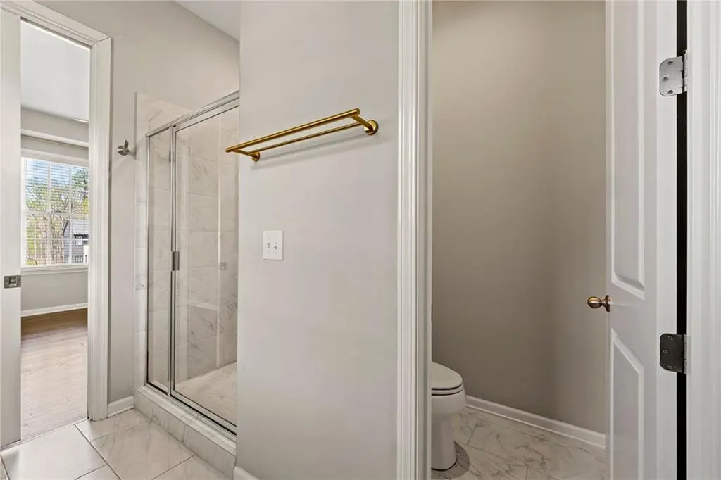 Bathroom featuring a shower stall, baseboards, marble finish floor, and toilet