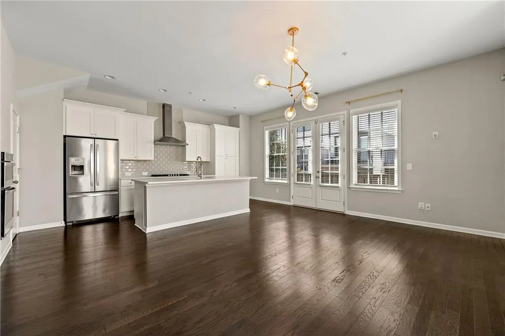 Kitchen with wall chimney exhaust hood, stainless steel appliances, dark wood-type flooring, backsplash, and a notable chandelier