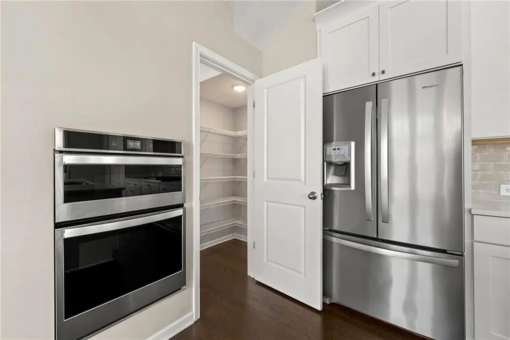 Kitchen with decorative backsplash, white cabinets, light countertops, stainless steel appliances, and dark wood-type flooring