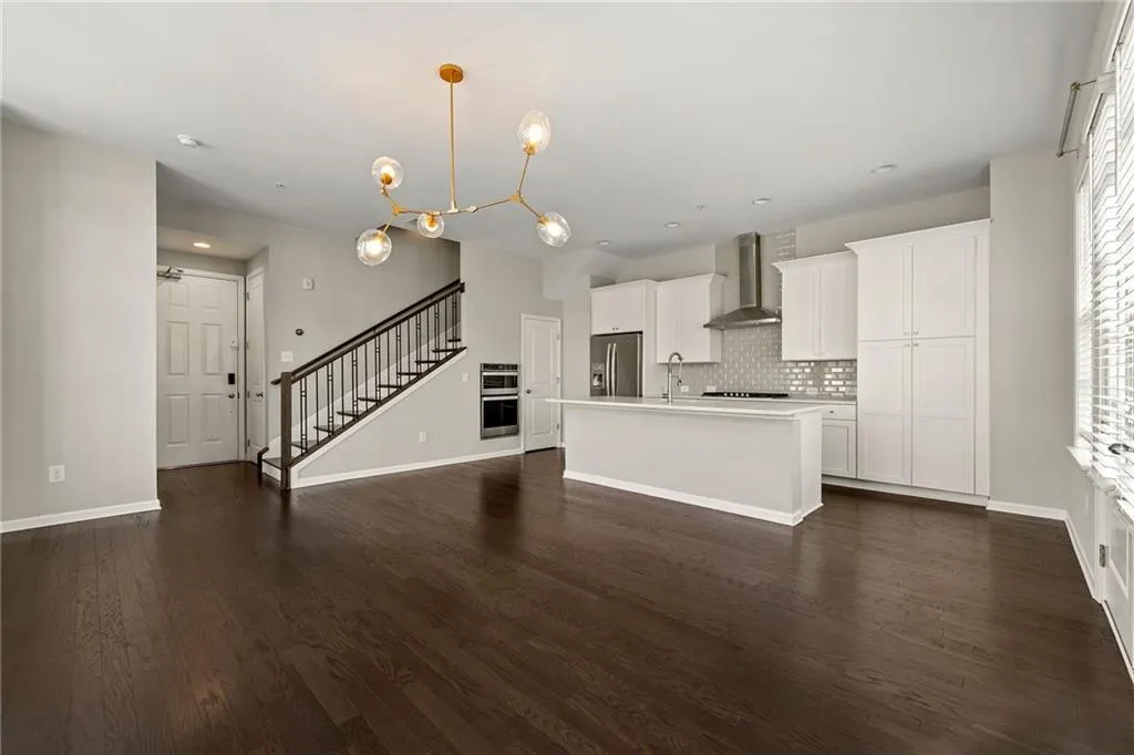 Kitchen with decorative backsplash, appliances with stainless steel finishes, an island with sink, dark wood-style floors, and wall chimney range hood