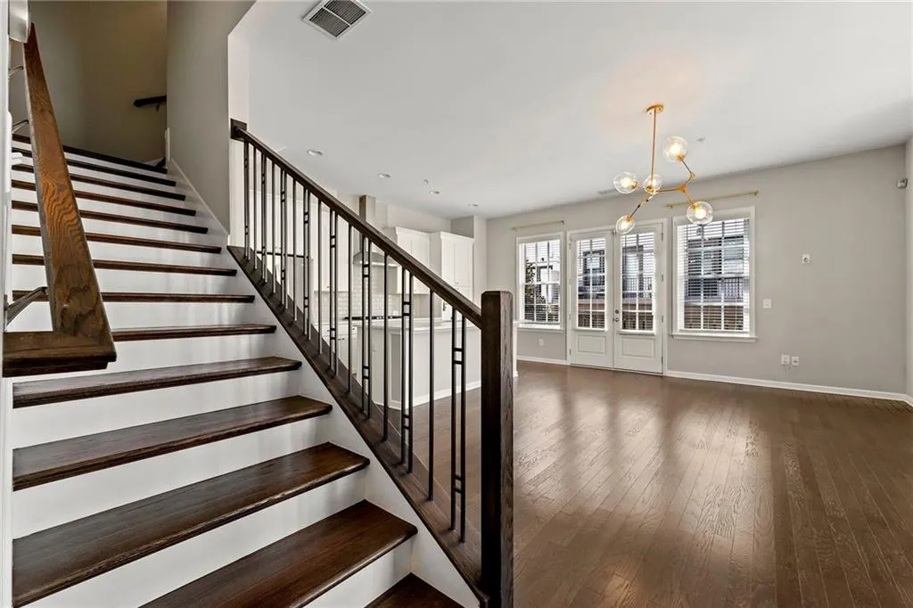 Stairway featuring hardwood / wood-style floors, baseboards, visible vents, and an inviting chandelier