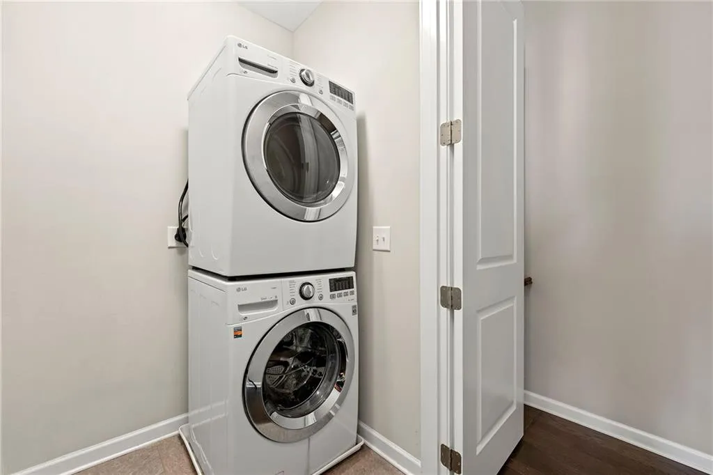 Clothes washing area featuring baseboards, wood finished floors, stacked washing maching and dryer, and laundry area