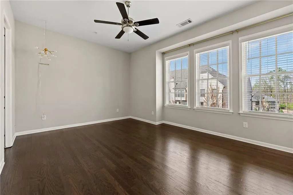 Empty room with dark wood-style flooring, ceiling fan with notable chandelier, baseboards, and visible vents